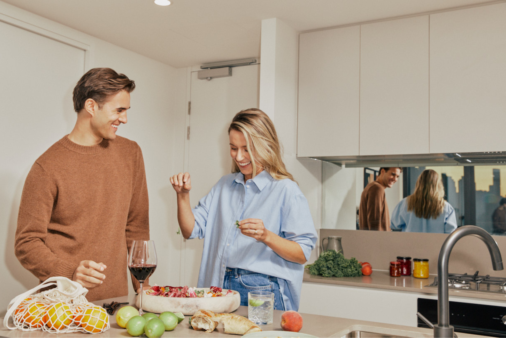 A man and woman stand in the kitchen, surrounded by food as they begin to plate a salad