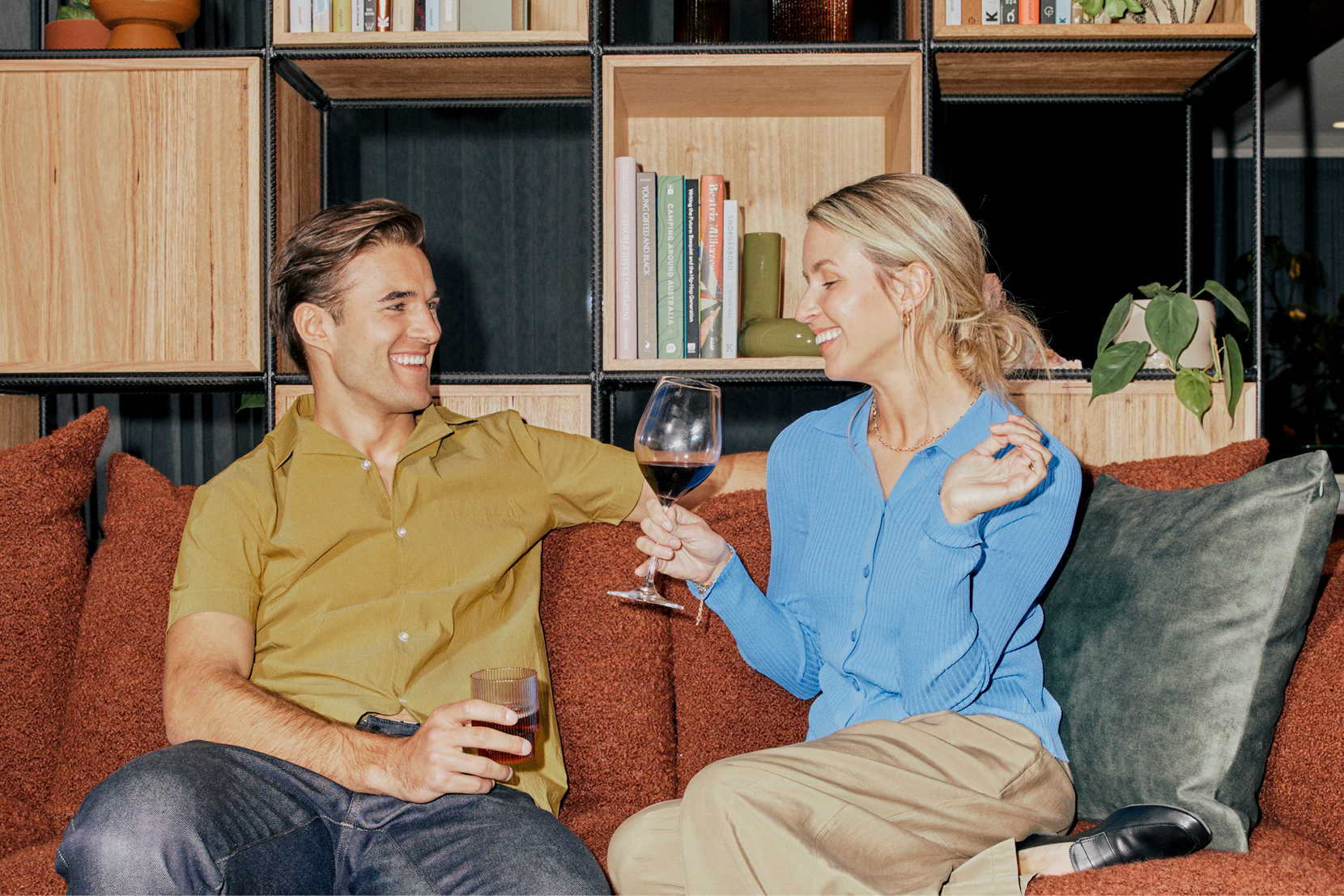 A man and woman sit on a couch laughing with a glass of wine.